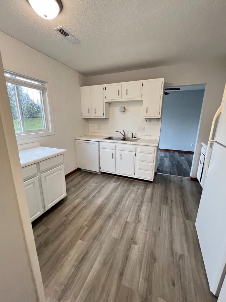 A kitchen with white cabinets , a refrigerator , a sink , and a window.