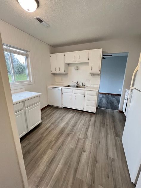 A kitchen with white cabinets , a refrigerator , a sink , and a window.