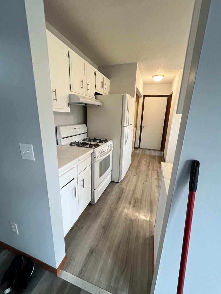 A kitchen with white cabinets , a stove , refrigerator , and microwave.