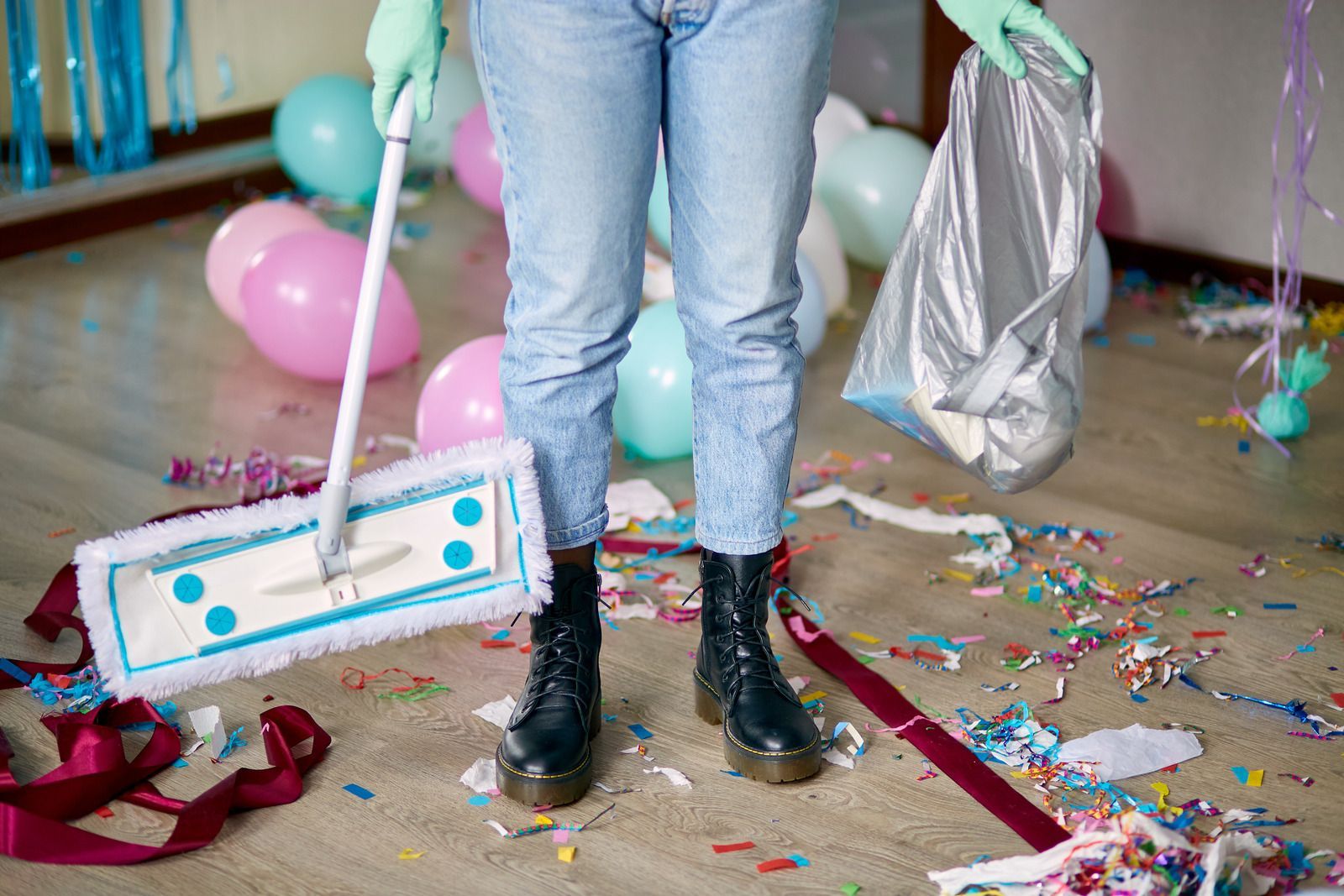 A person is cleaning a messy room with balloons and confetti.