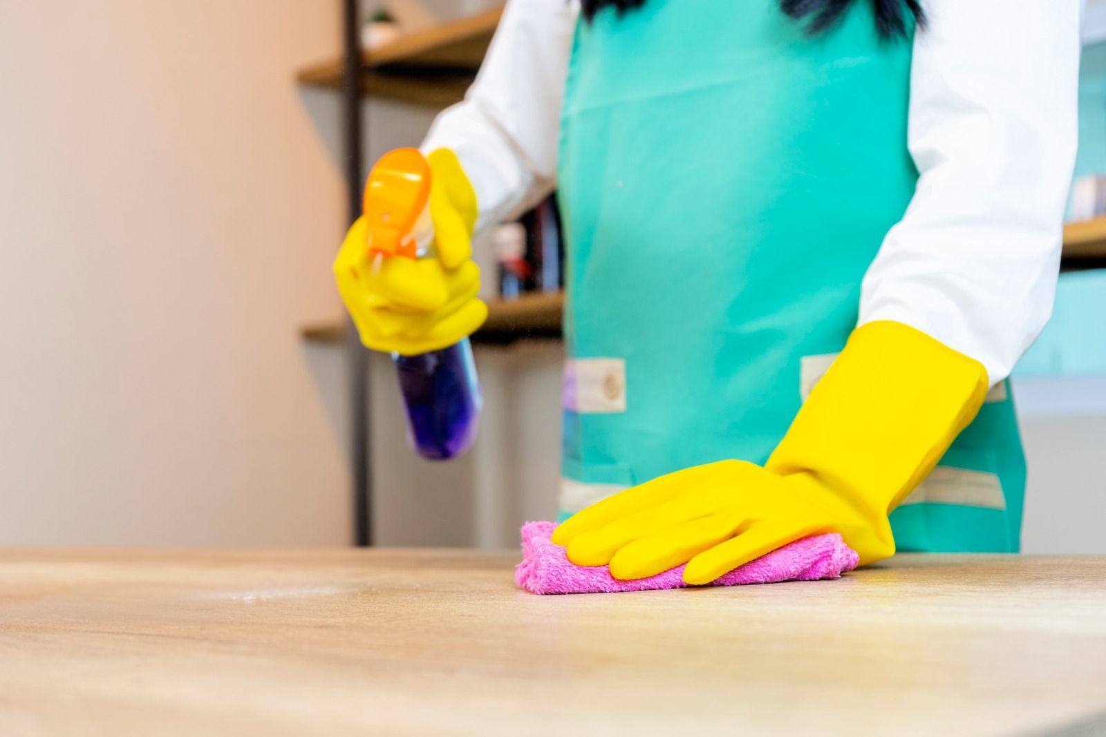 A woman wearing yellow gloves is cleaning a wooden table with a cloth.