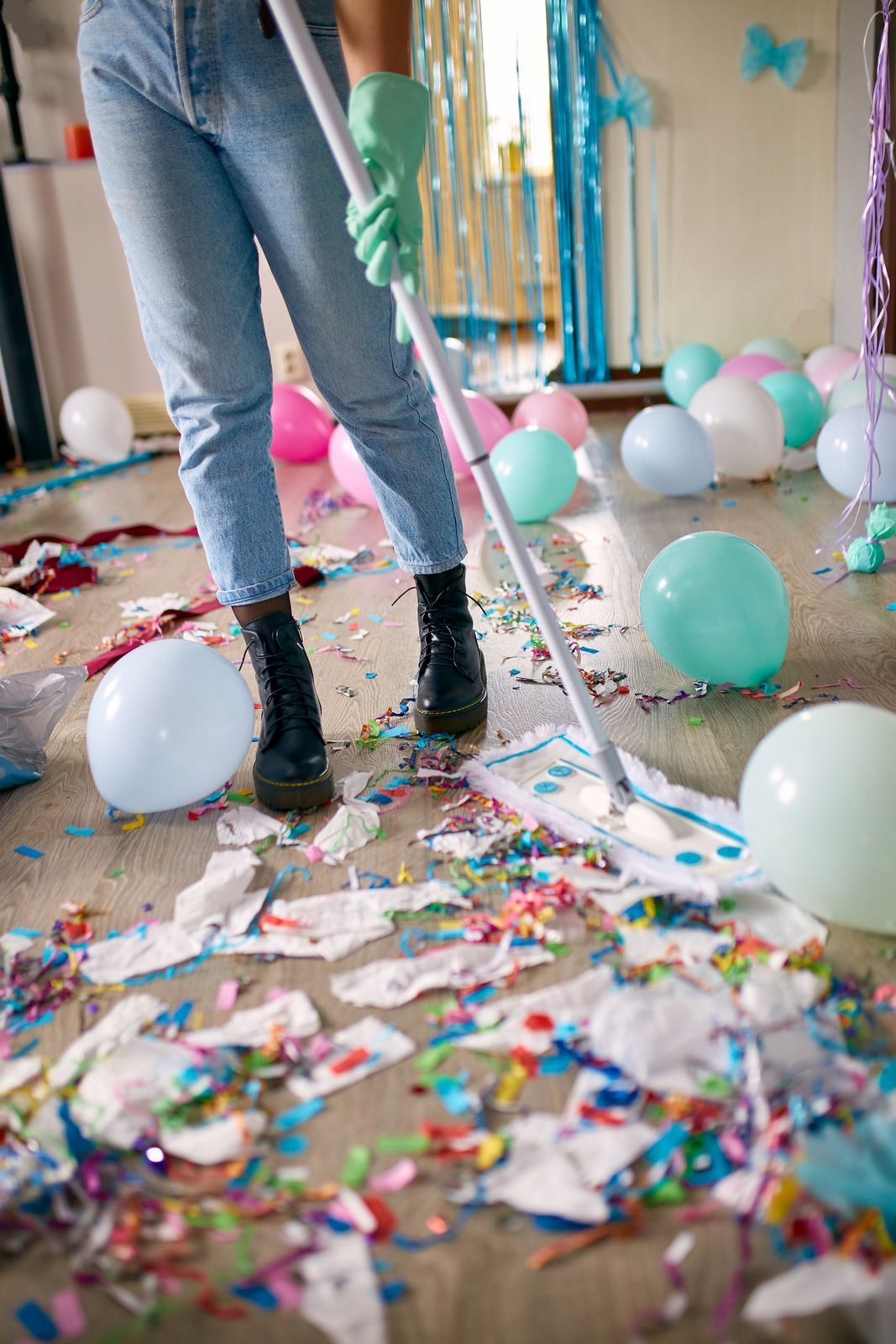 A woman is cleaning the floor of a messy room with balloons and confetti.