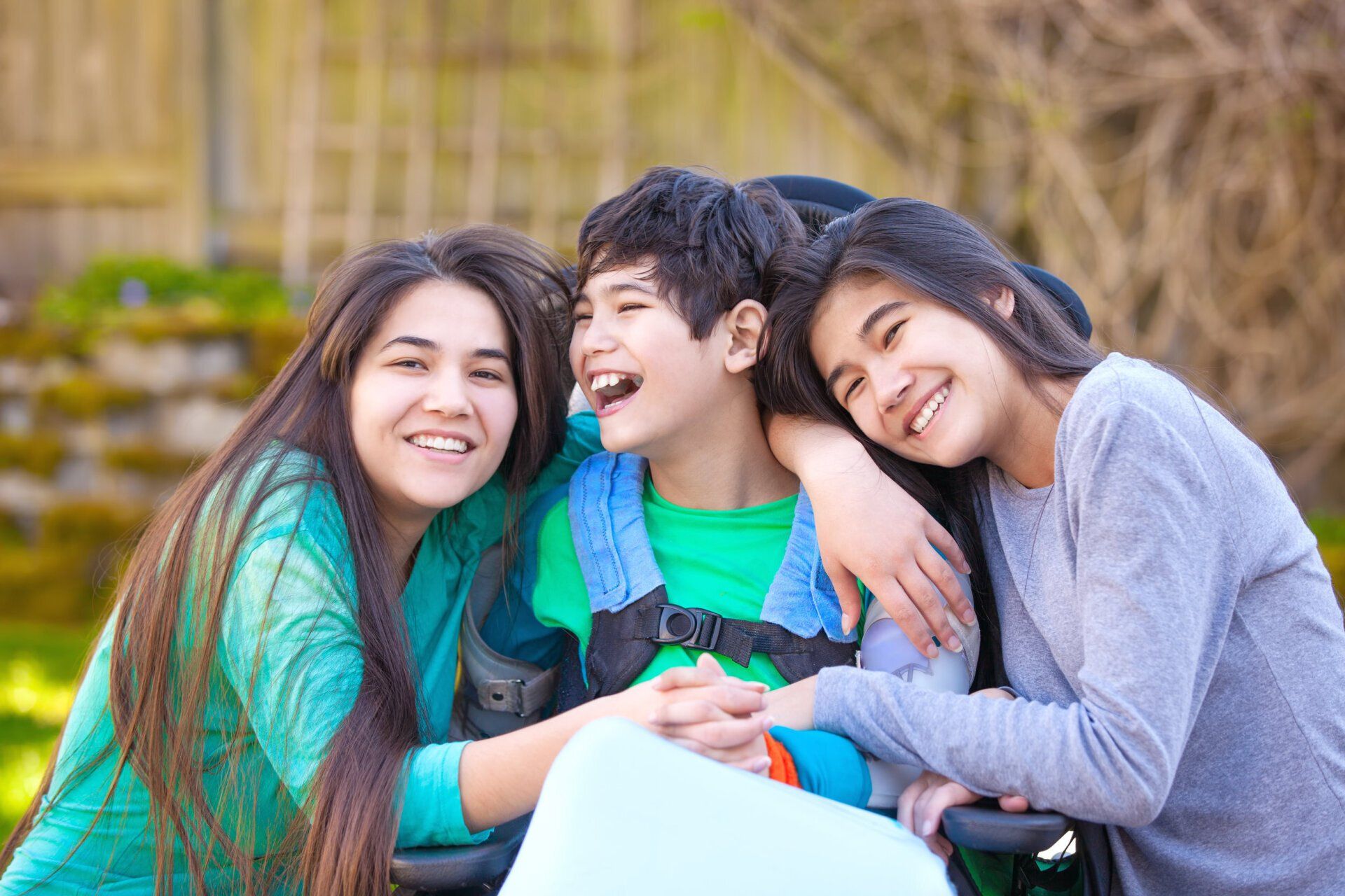 Two girls are hugging a boy in a wheelchair.