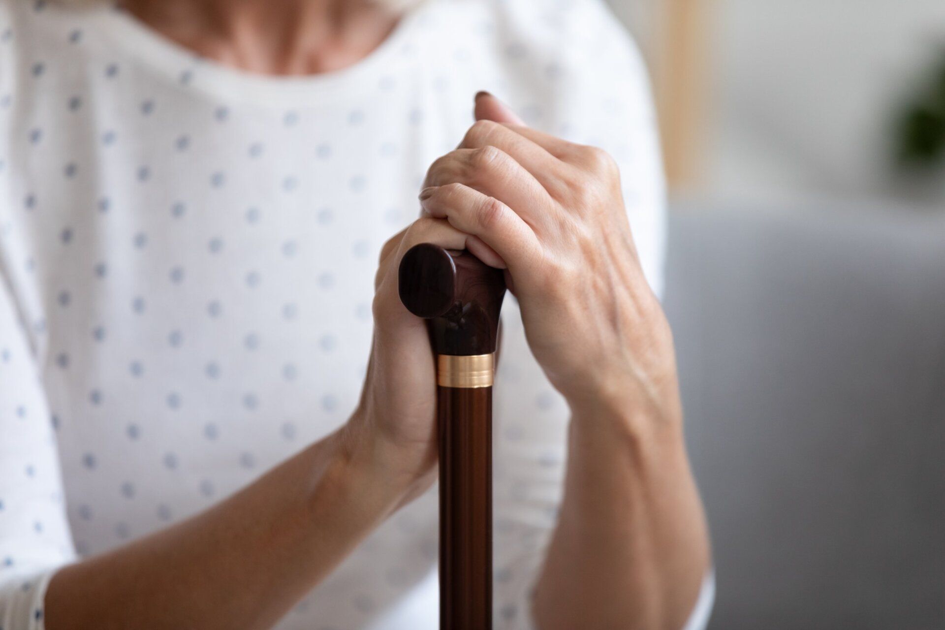 An elderly woman is holding a cane in her hands.