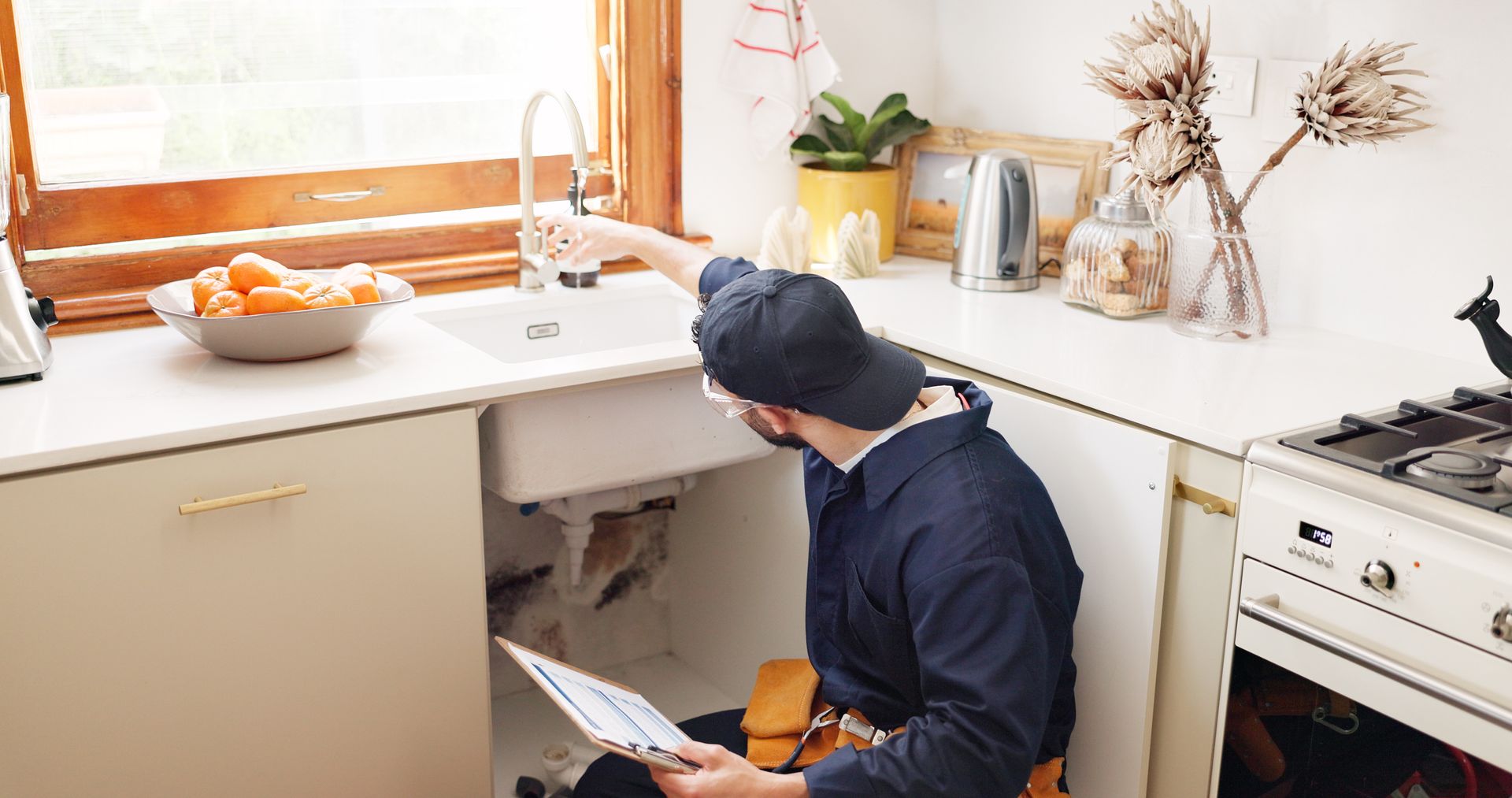 A plumber is fixing a sink in a kitchen.