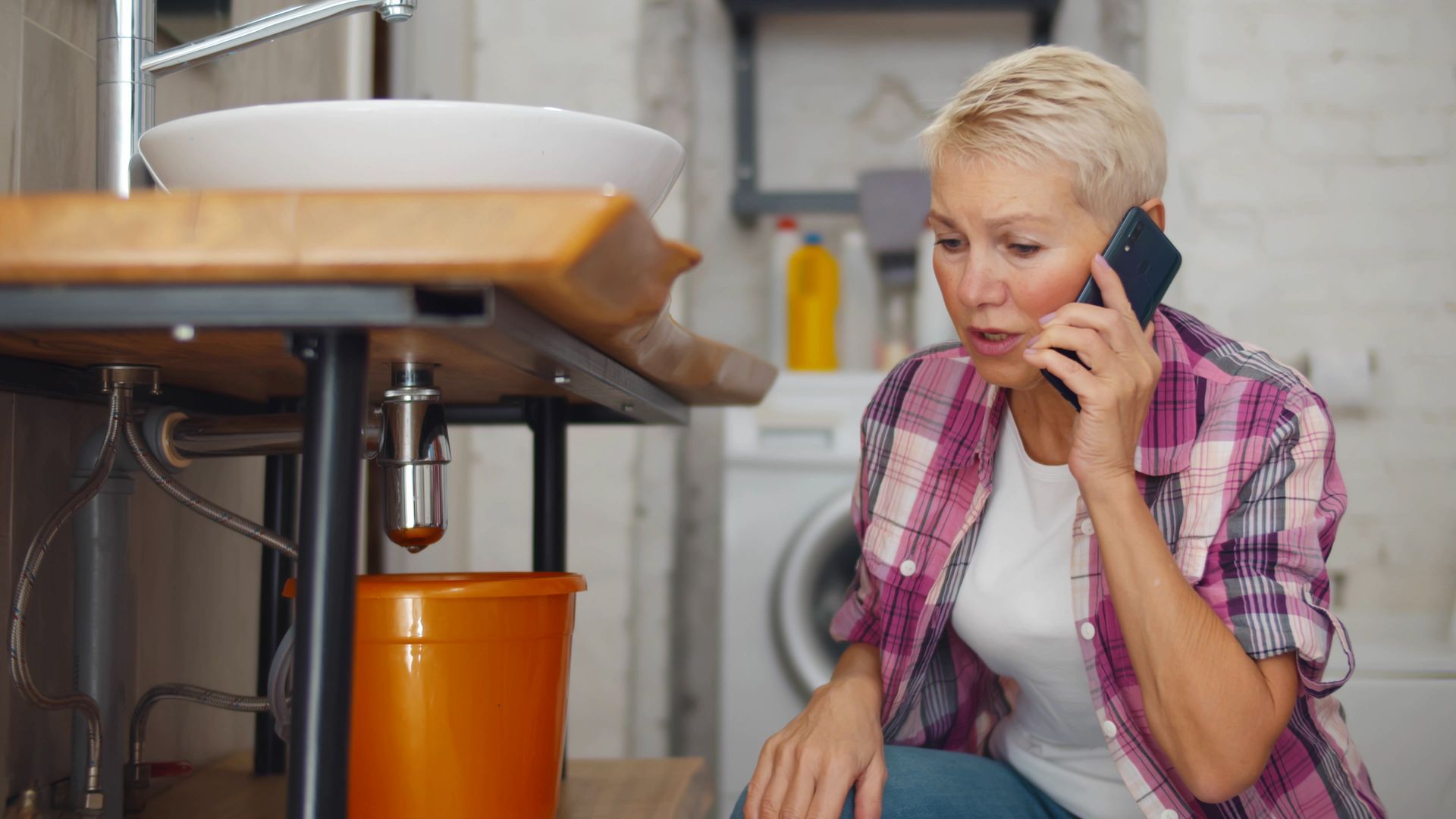 A woman is talking on a cell phone in front of a sink in a bathroom.