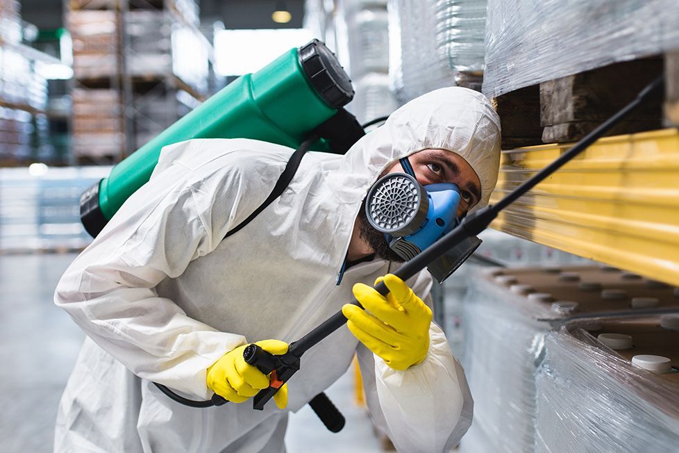 A man in a protective suit is spraying a warehouse with a sprayer.