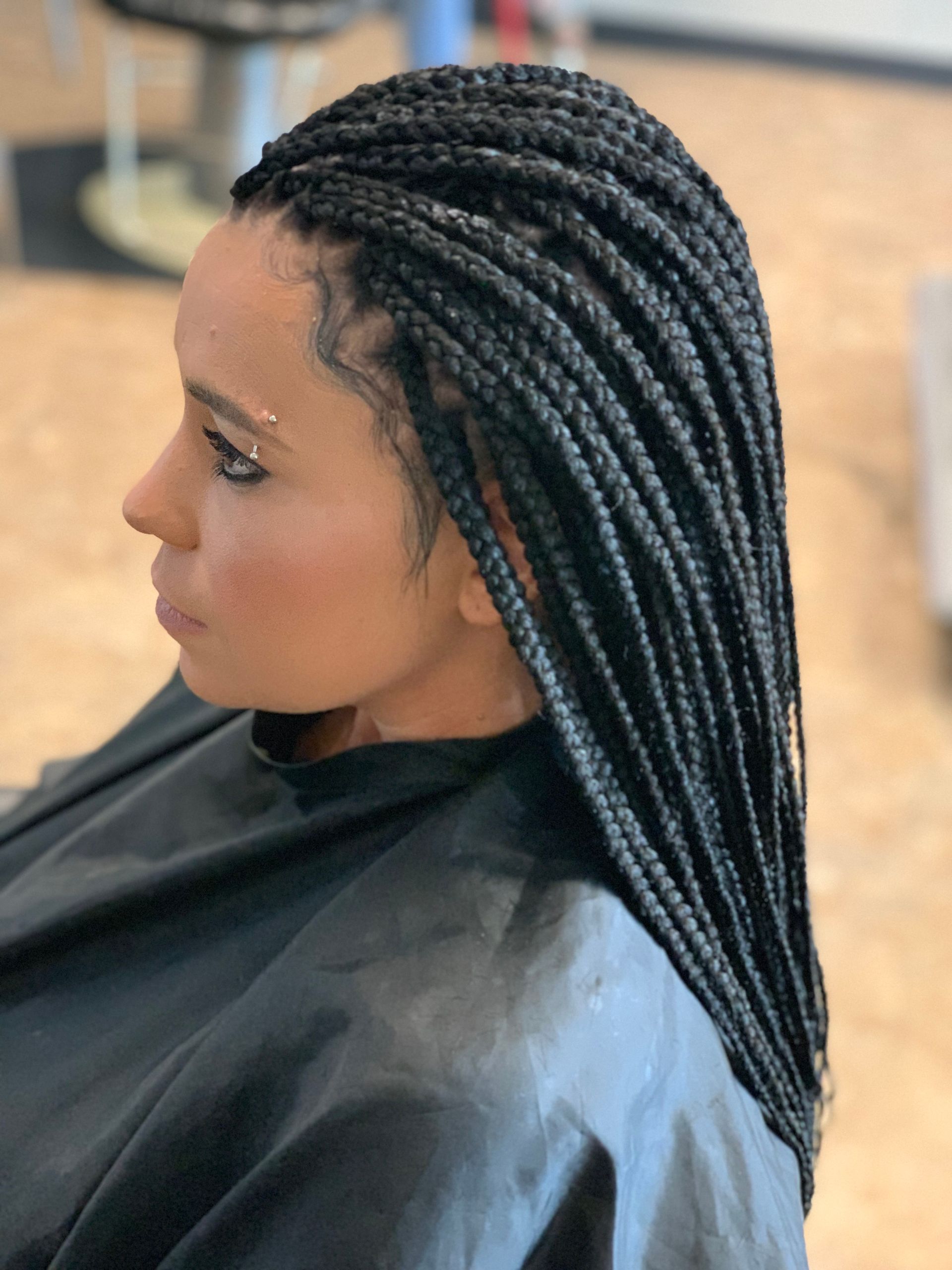 Woman with black box braids, side profile, indoors. Wearing a black cape.