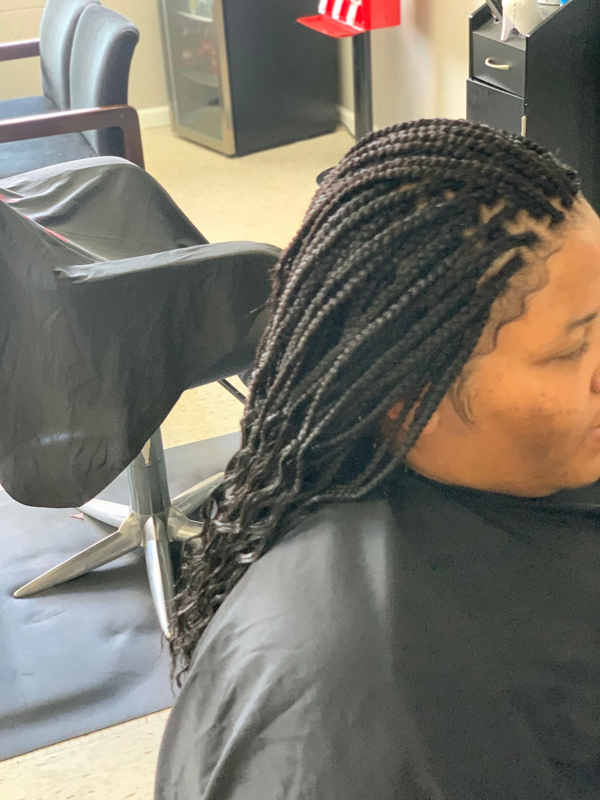 Woman with long box braids at a salon. Braids are dark brown/black, with some falling down her shoulder.