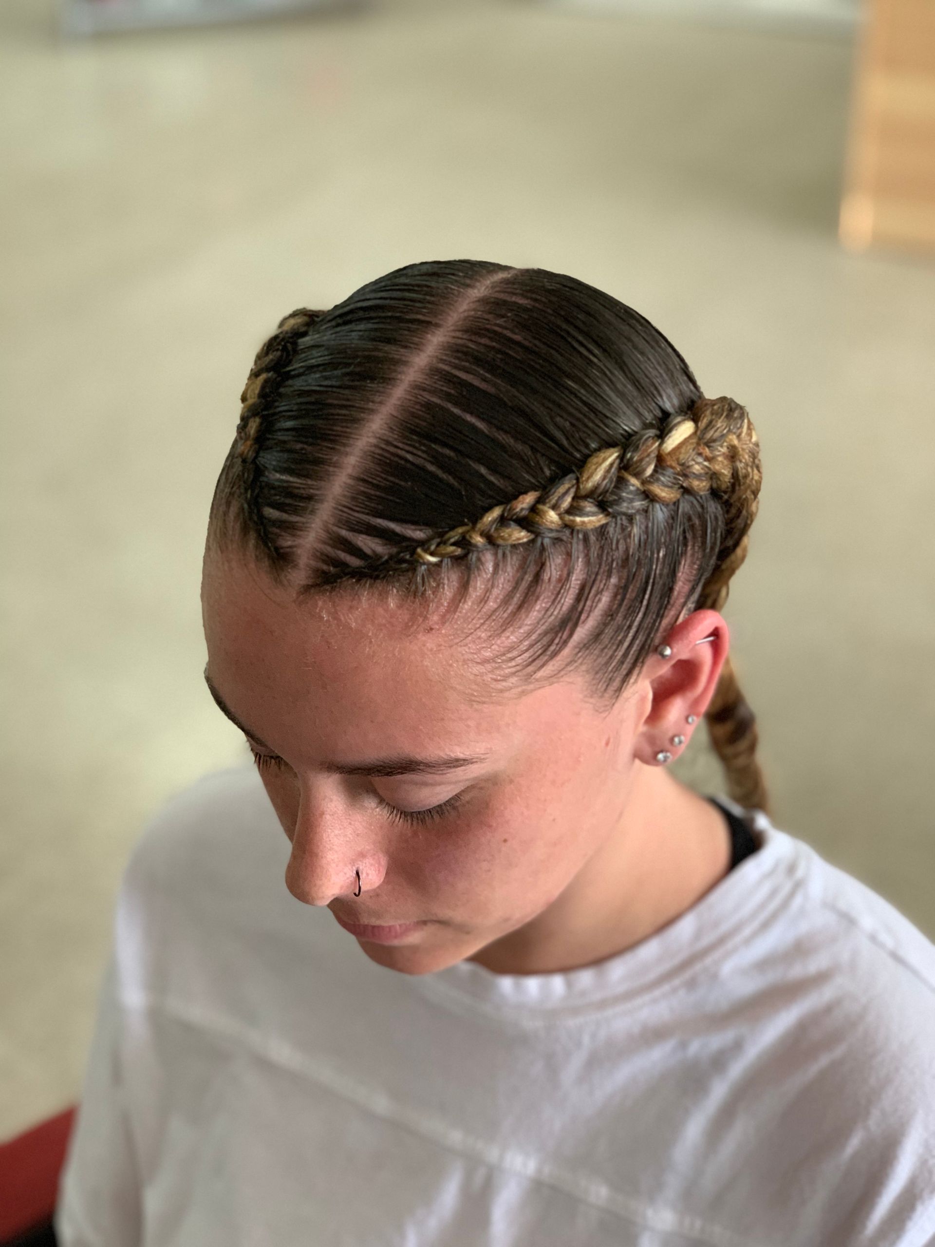 A person with two braided pigtails, braided around their head, wearing a white shirt.