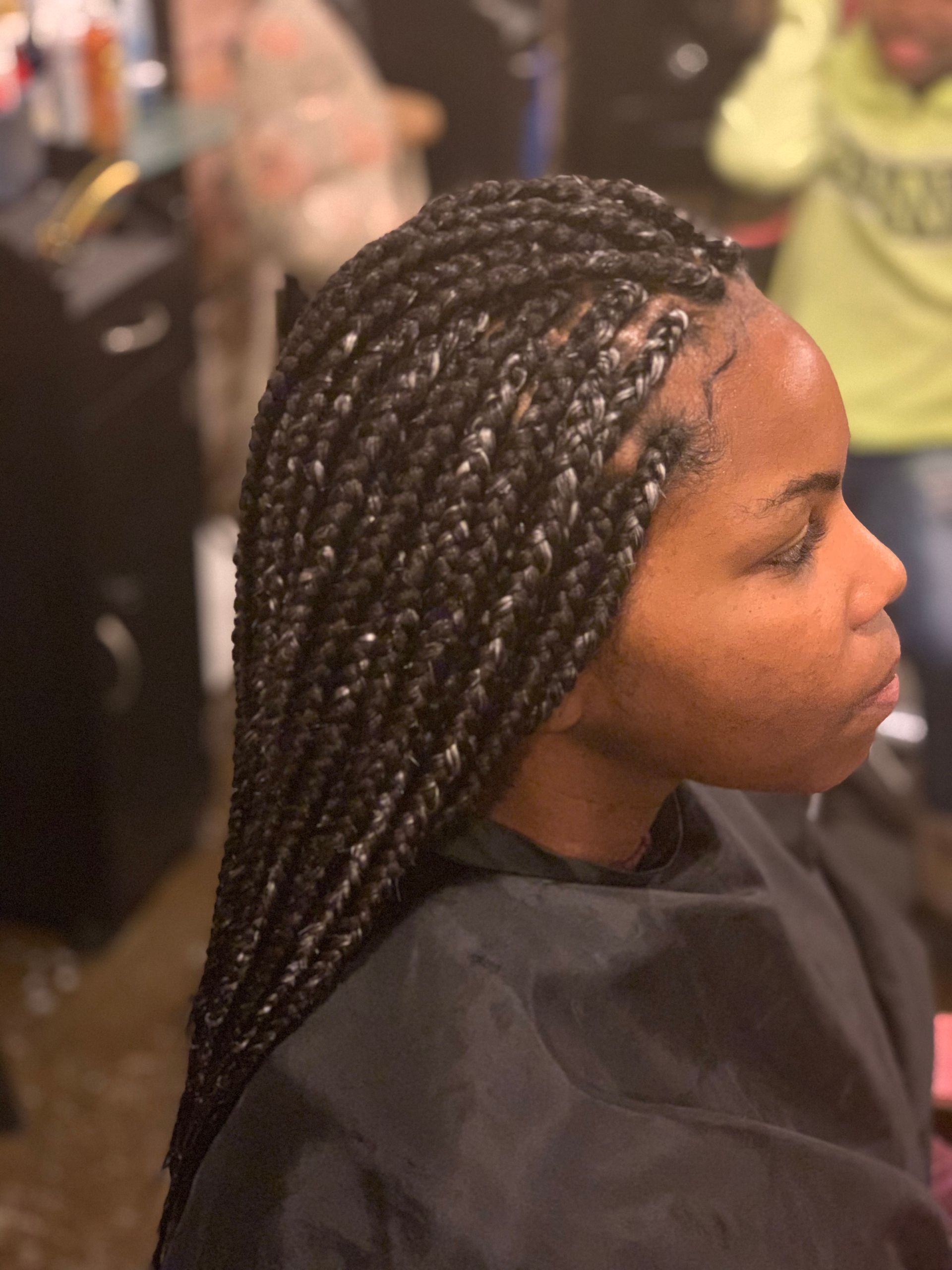 Woman with black box braids, profile view. Indoors, wearing a black cape.