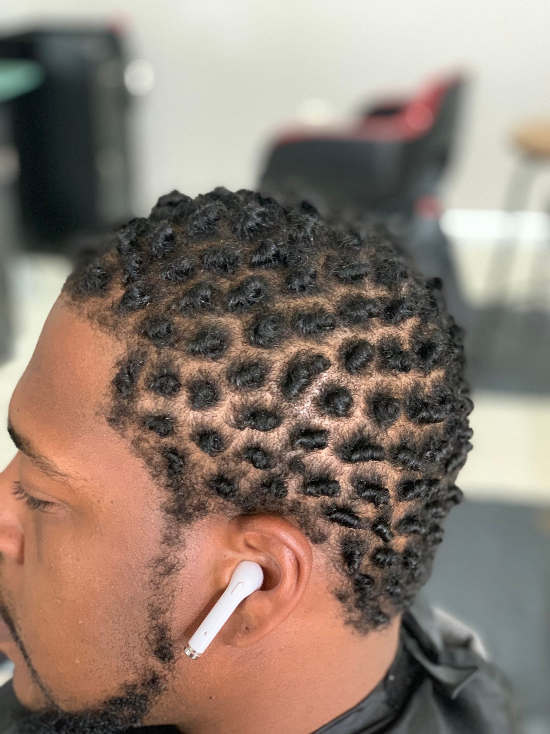 Man with dark skin wearing an AirPod, sporting a short, textured hairstyle, in a salon.
