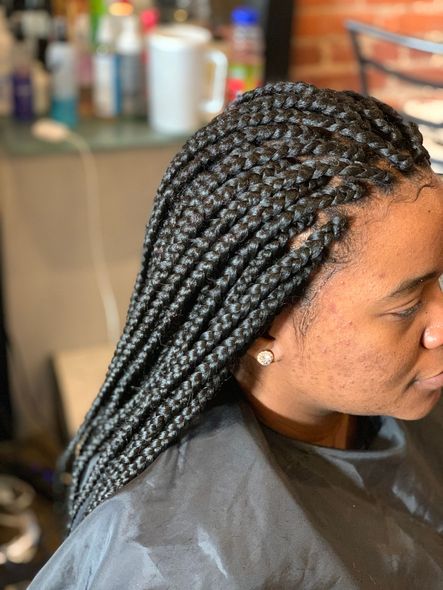 Woman with black box braids in a salon, wearing a black cape.