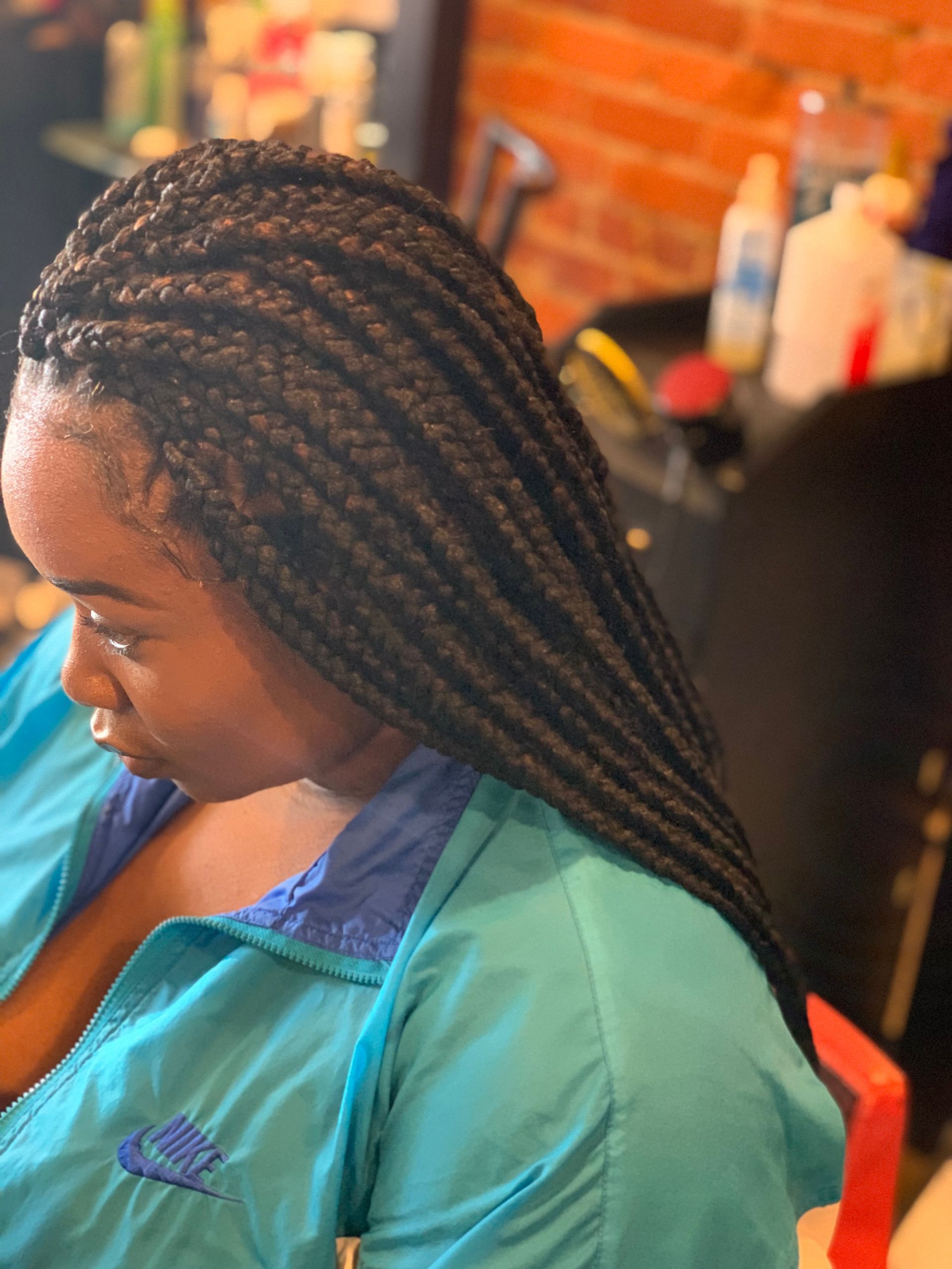 Woman with long, black box braids wearing a turquoise jacket, sitting in a salon.