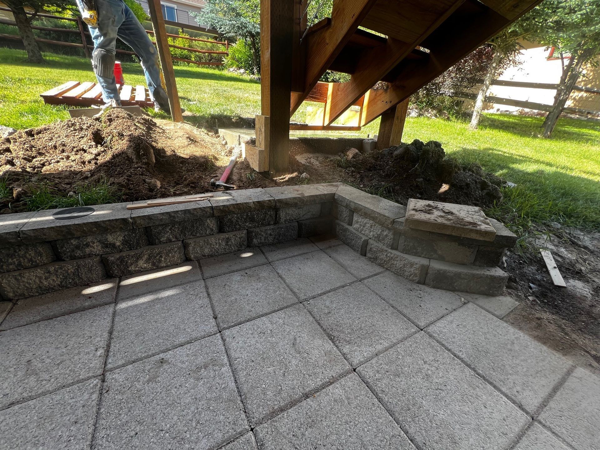 A man is working on a patio under a wooden deck.