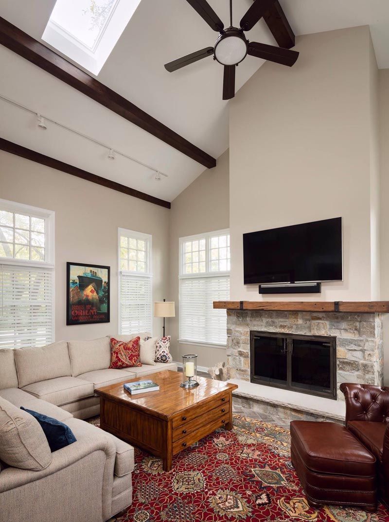 Living room with fireplace, sectional sofa, and wooden coffee table. Beige walls, red rug, high ceiling with beams.