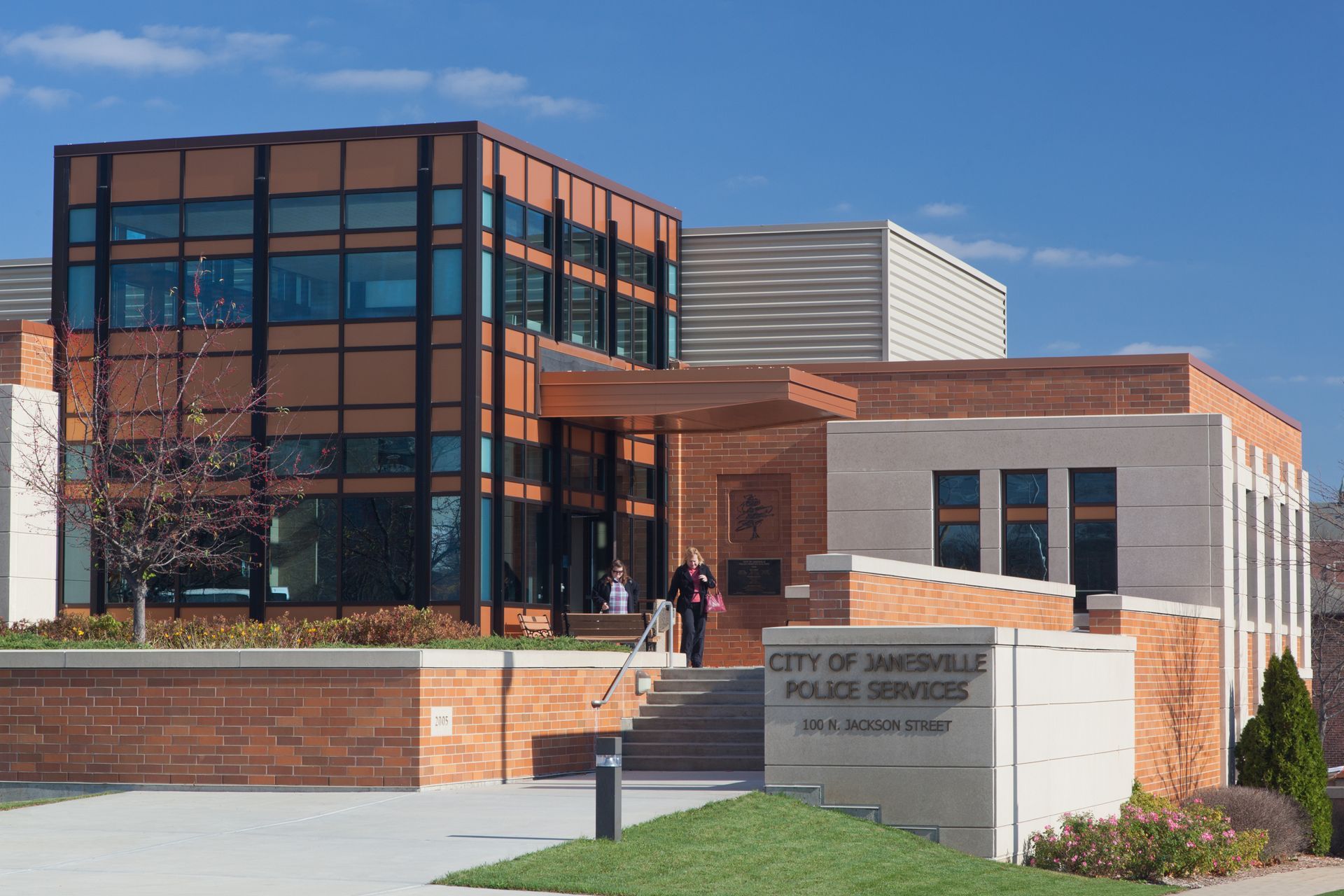 City of Janesville Police Services building with brick and glass exterior; people are present.