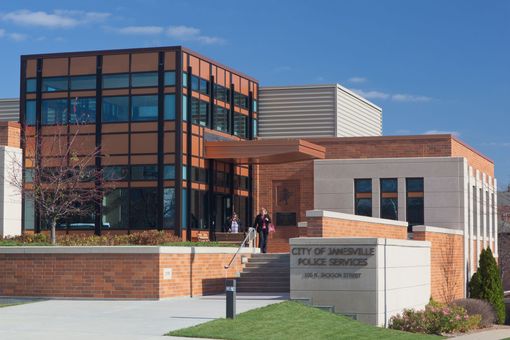 City of Janesville Police Services building with brick and glass exterior; people are present.