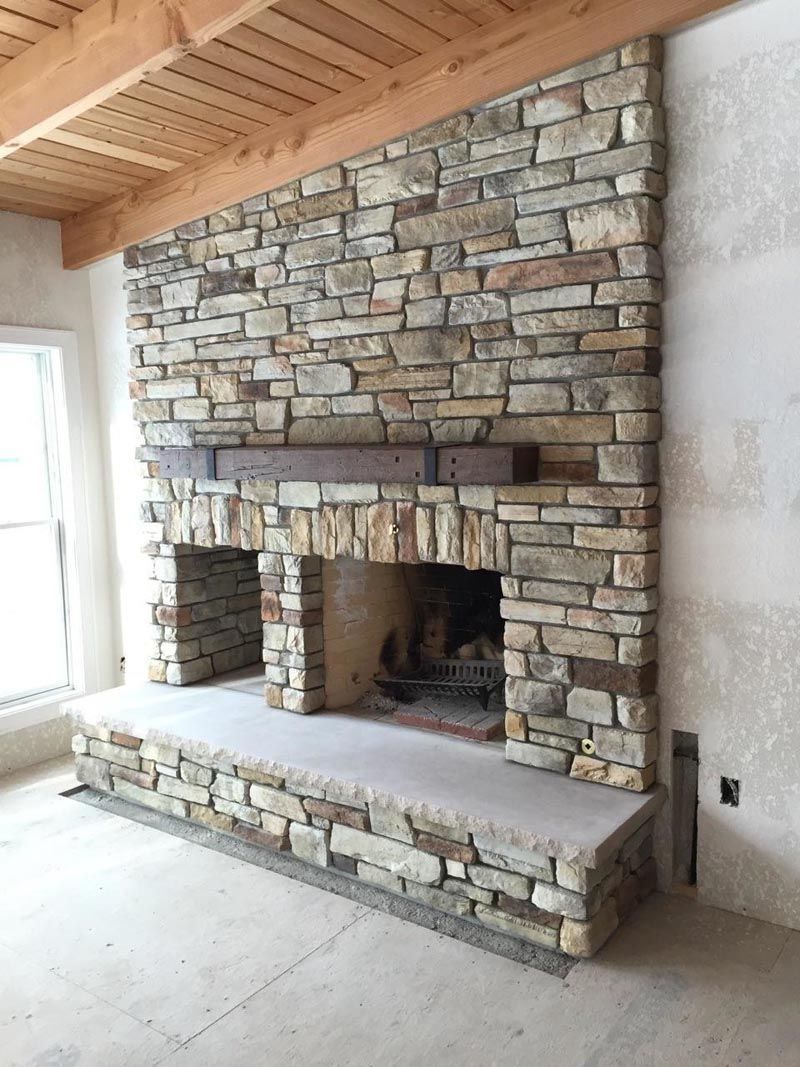 Stone fireplace with a wooden mantel, in a room under construction.