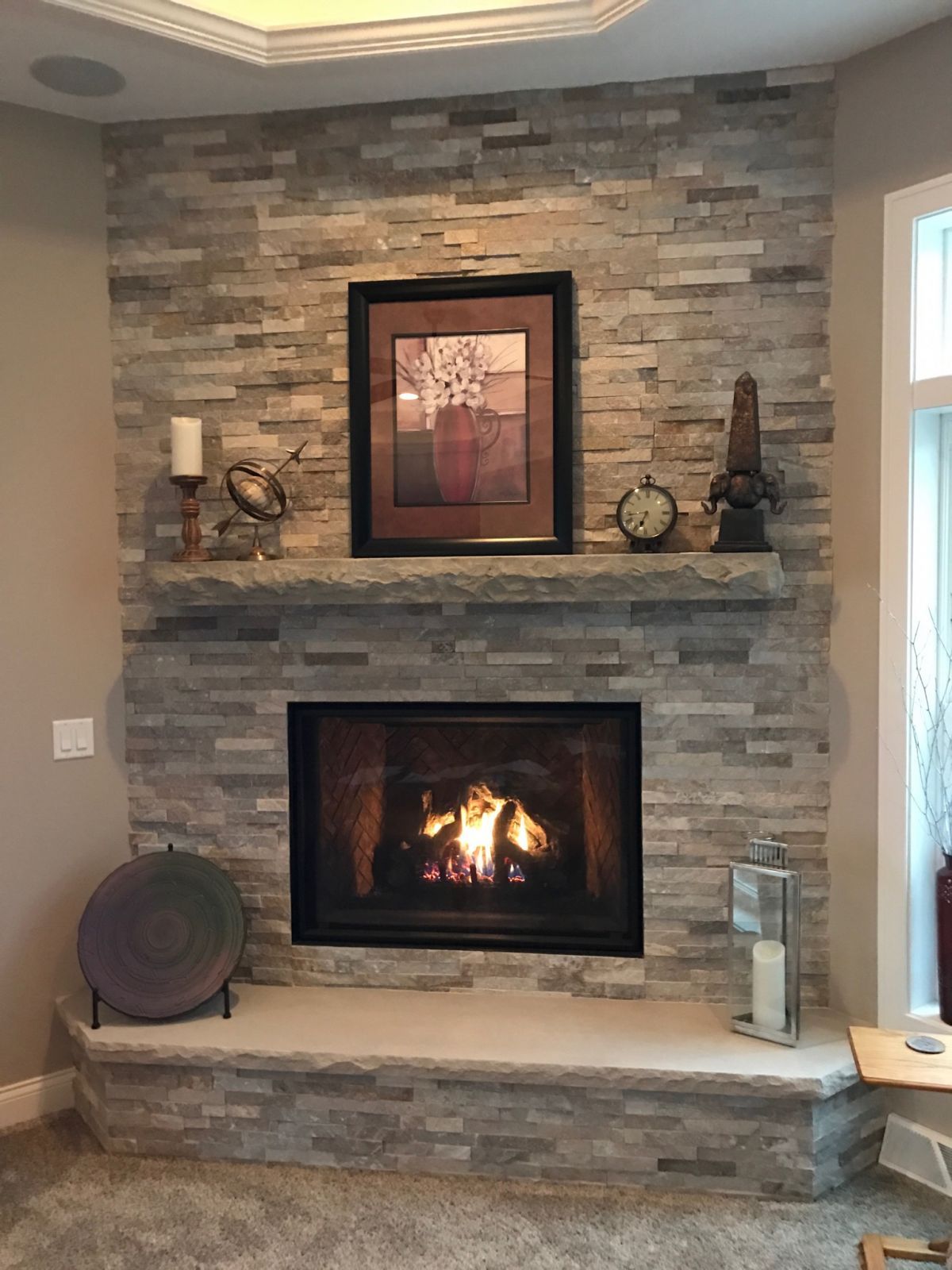 Fireplace with stone surround, mantle, and decorative items; artwork, candles, and clock.