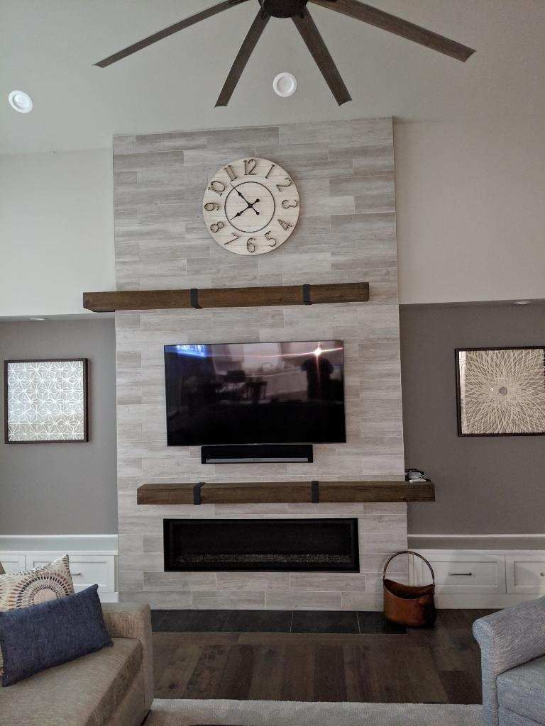 Living room with fireplace, TV, and clock on a tiled wall, brown shelves and a ceiling fan.