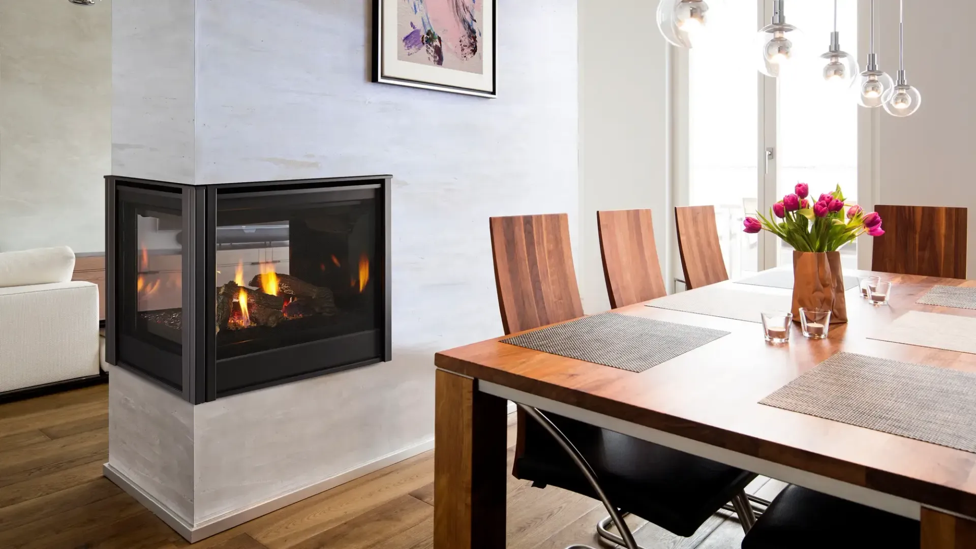 Corner fireplace in modern dining room with wooden table and chairs, flowers, and artwork.
