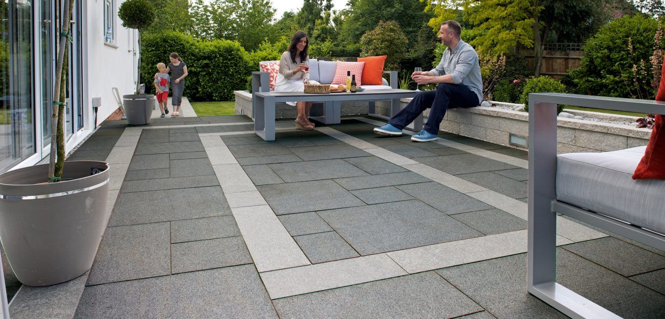 Family enjoying patio: gray pavers, outdoor furniture, garden, couple, children, sunny day.