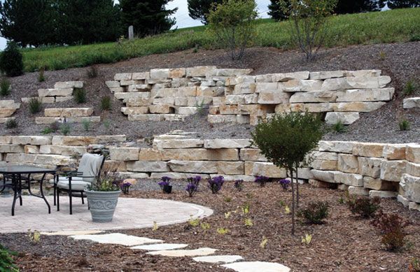 Stone retaining walls on a hillside with a patio, plants, and a table.
