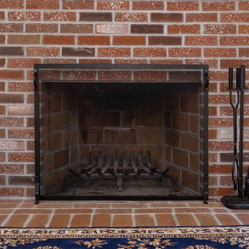 Brick fireplace with black screen and tools; blue patterned rug in front.