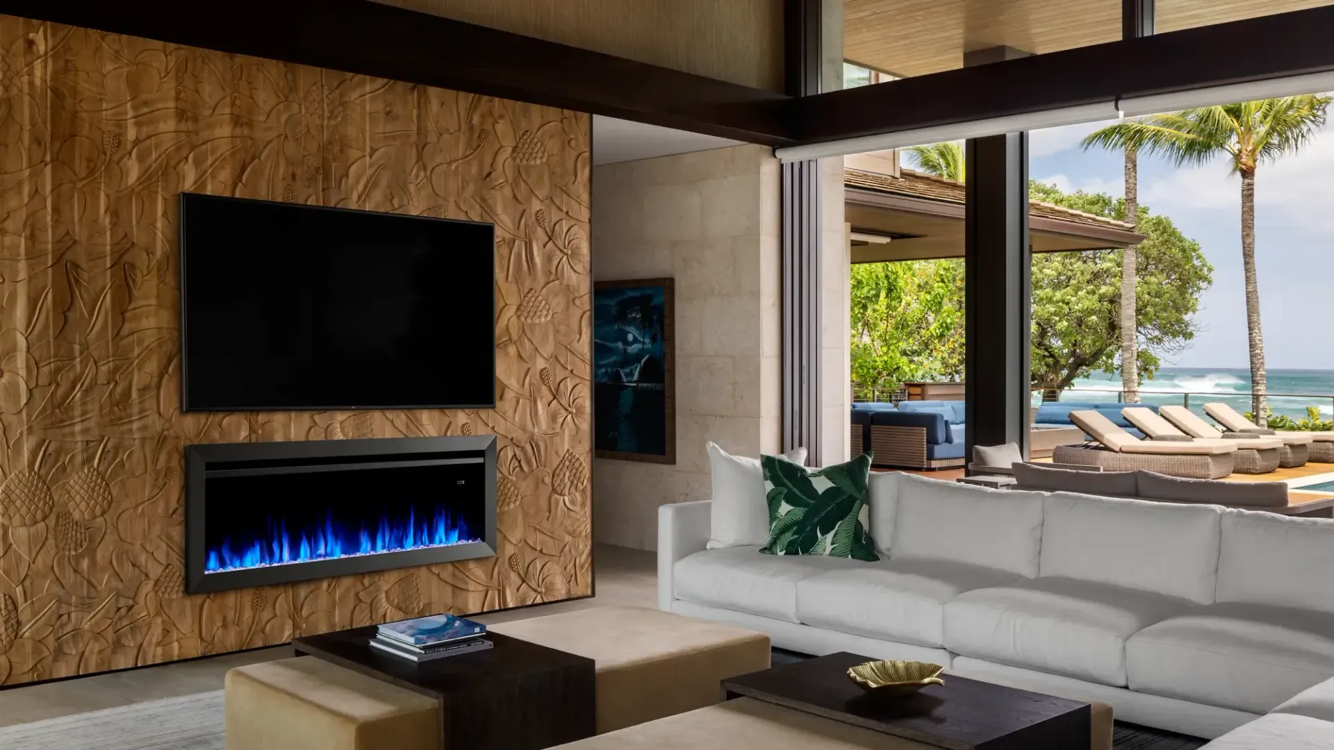 Modern living room with fireplace, TV, and ocean view. White couch, wood paneling, palm trees.