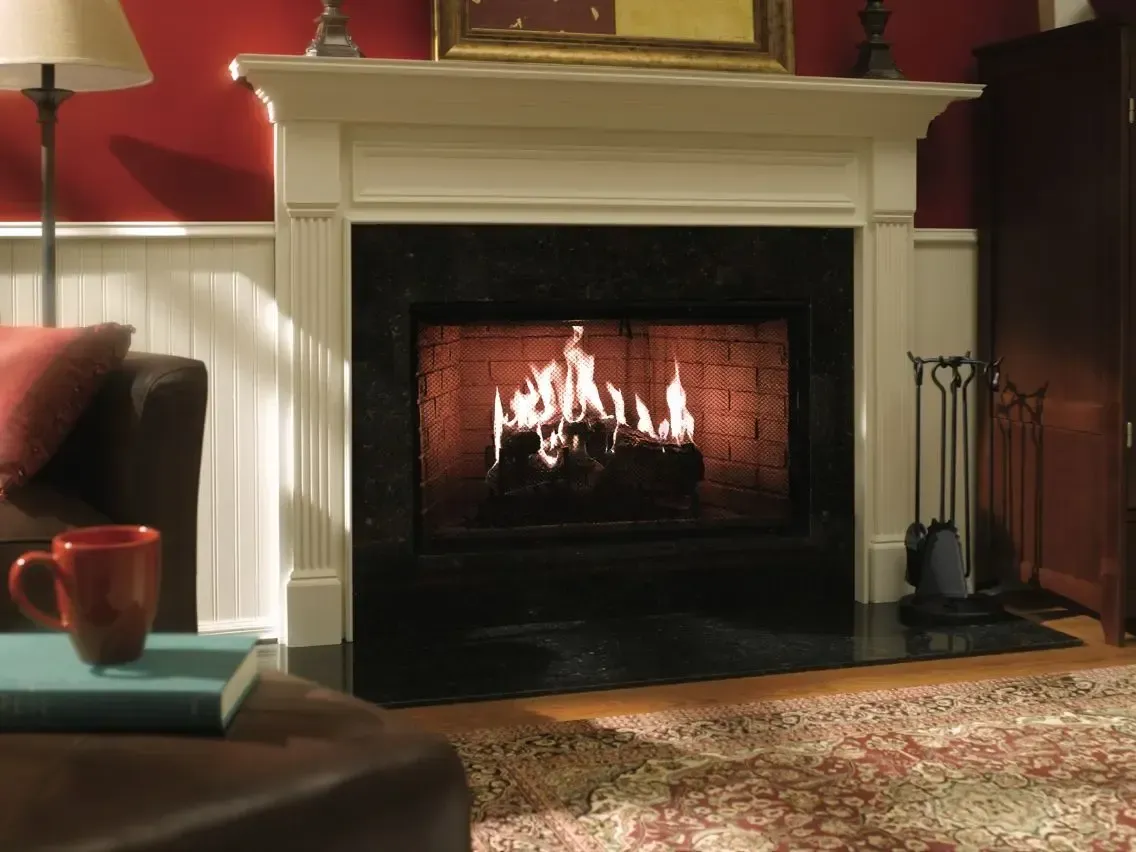 Fireplace with a burning fire, white mantel, and dark granite surround. Cozy living room with red wall.
