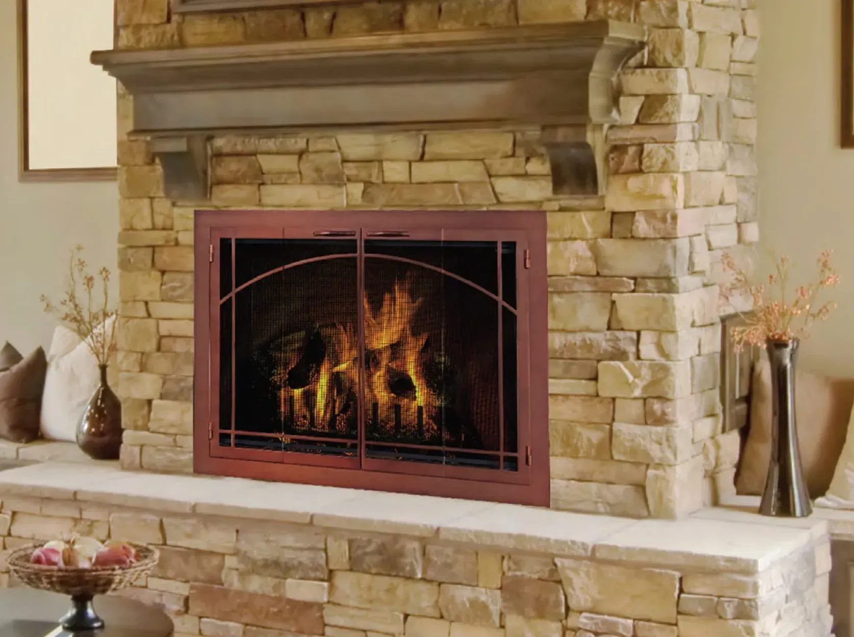 Fireplace with stone surround, flames visible behind brown framed doors.