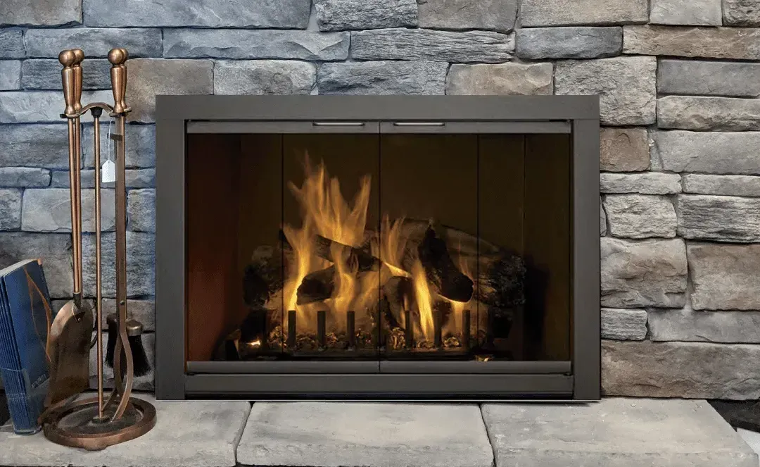 Fireplace with burning logs, set in a stone wall, with copper fireplace tools.
