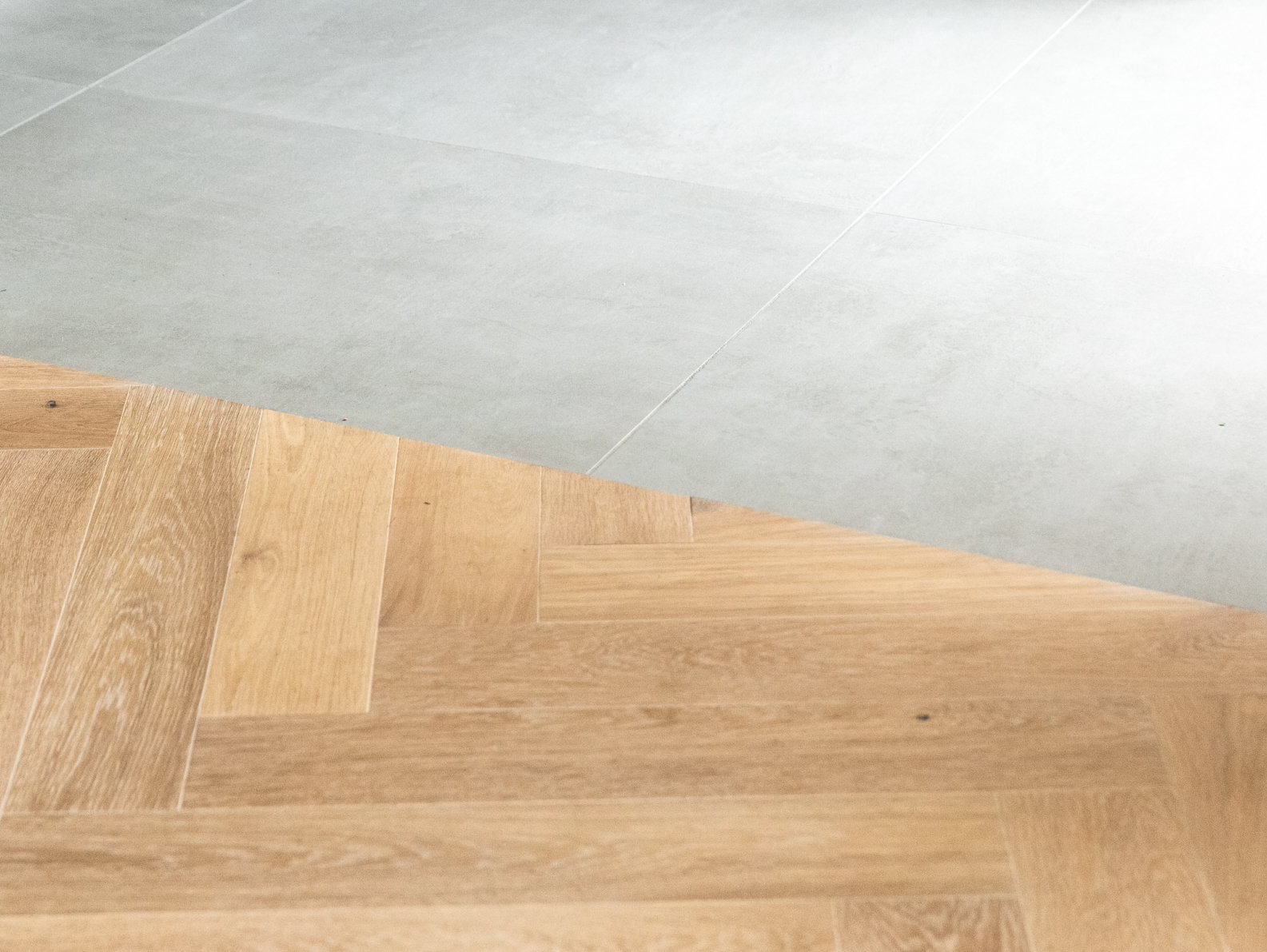 Twee soorten vloeren combineren. Een houten visgraat vloer in combinatie met een tegelvloer.