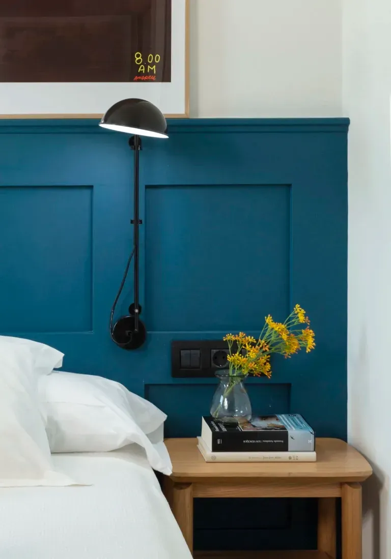 A bed with a blue headboard and a nightstand with a vase of flowers on it.