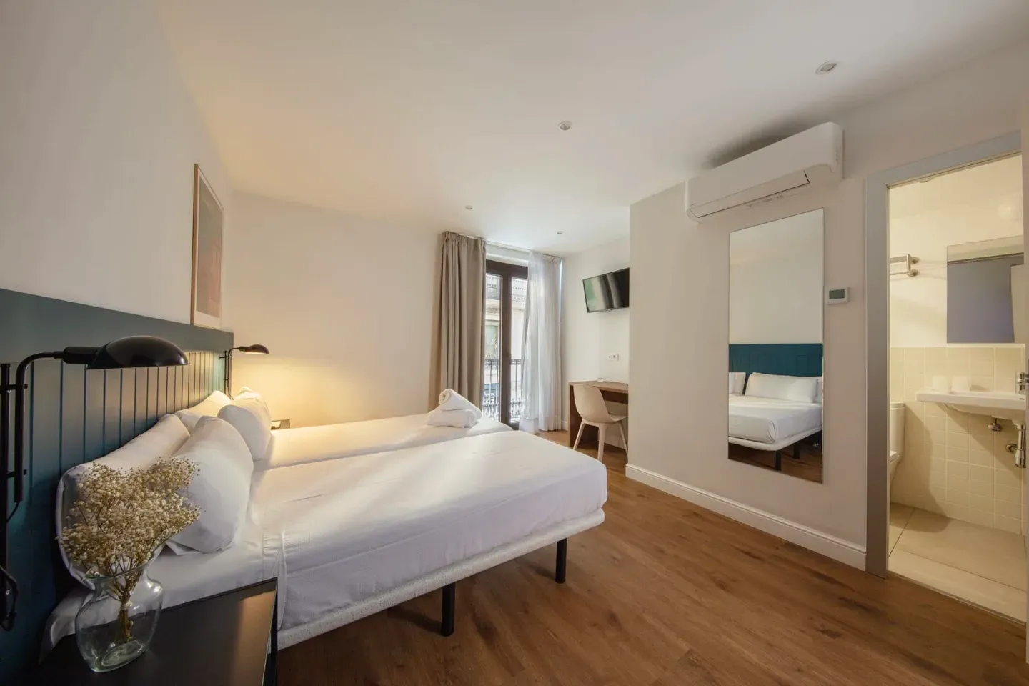 A hotel room with two beds , a sink and a mirror.