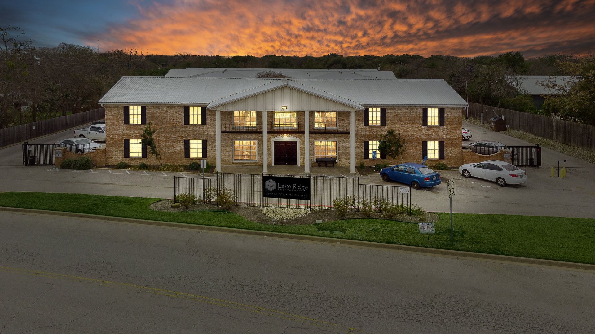 An aerial view of a large brick building with cars parked in front of it at sunset.