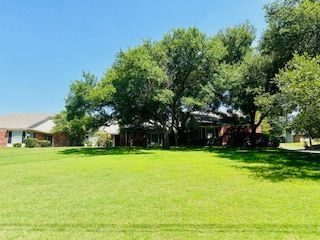 A house with a large lawn in front of it surrounded by trees.