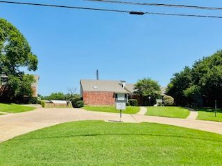 A brick house is surrounded by lush green grass and trees.