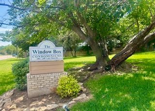 A sign for the window box condominiums is in the middle of a lush green field.