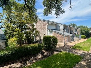 A large apartment building with a walkway leading to it surrounded by trees and bushes.