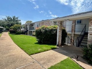 A brick apartment building with stairs and a lush green lawn.