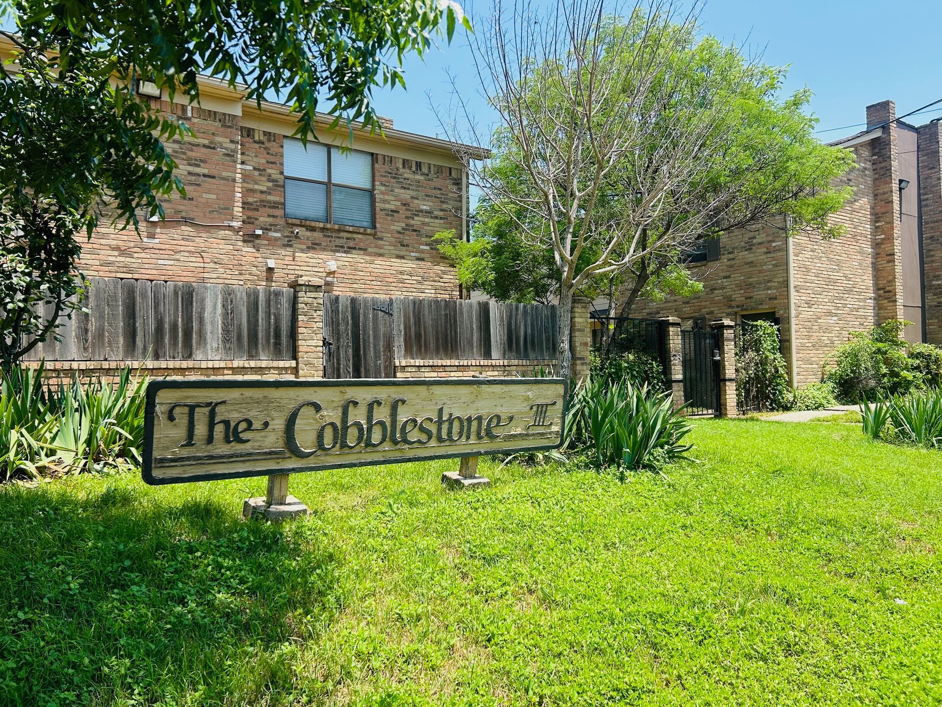 A sign for the cobblestone apartment complex is in front of a brick building.