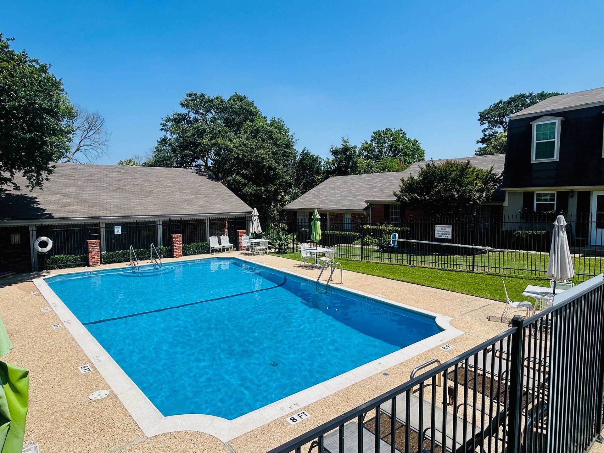 A large swimming pool is surrounded by a fence and houses.