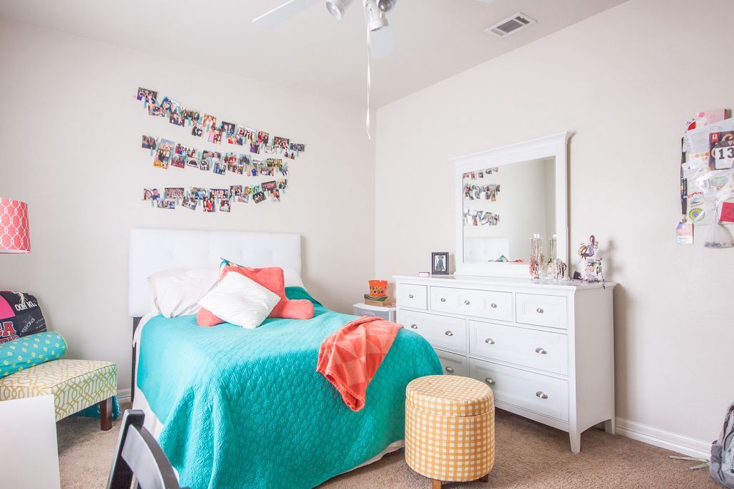 A bedroom with a bed , dresser , mirror and ottoman.