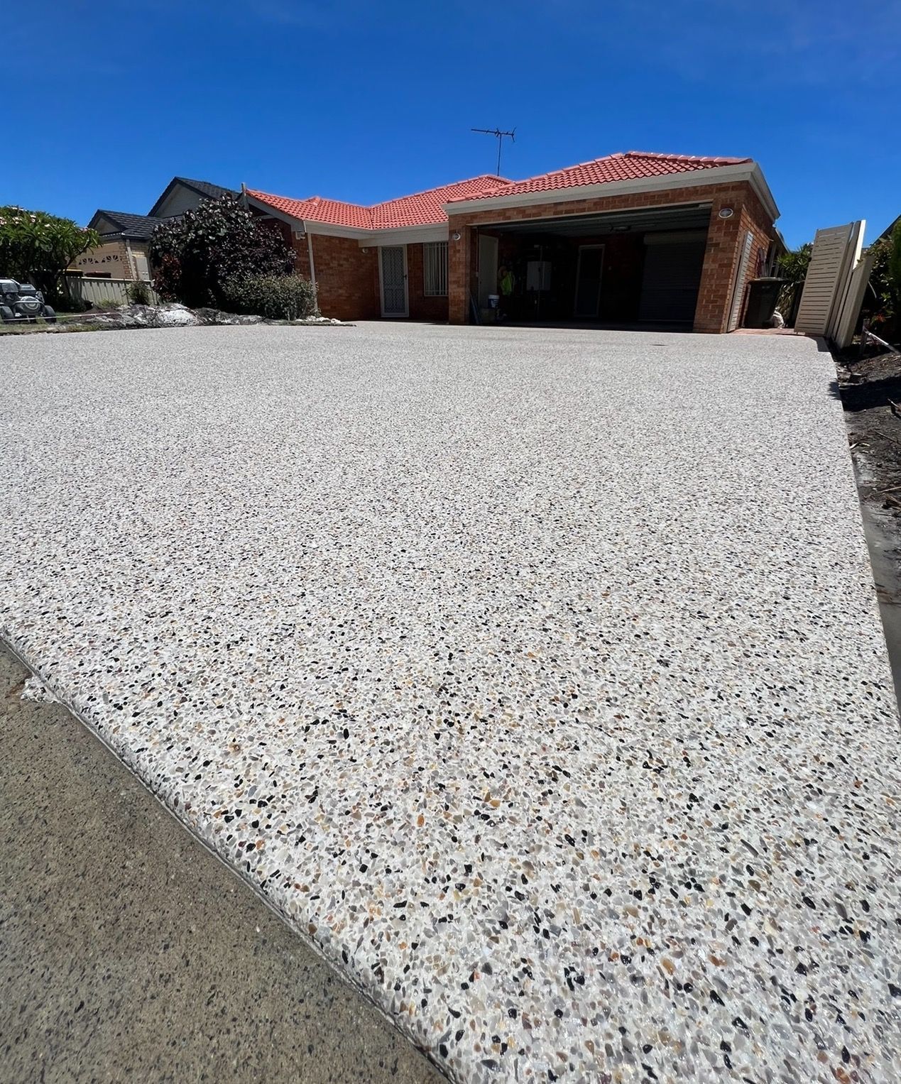 Exposed aggregate driveway with light coloured aggregates leading to home with red roof.