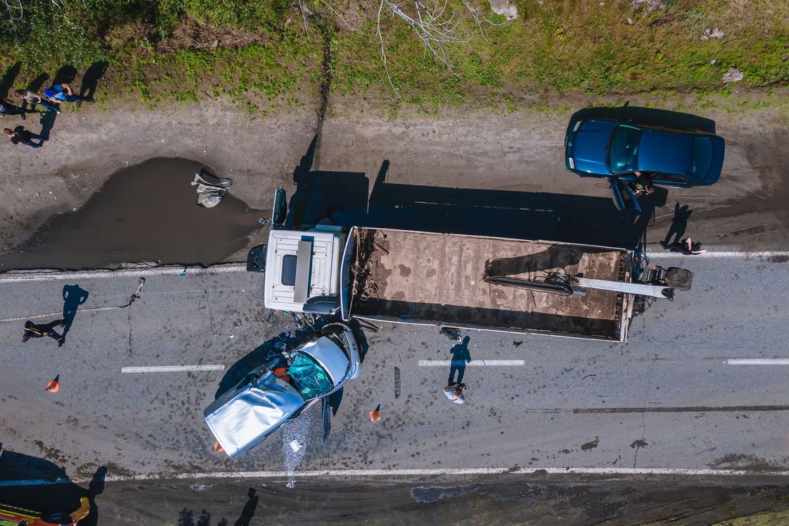 Aerial view of a road crash with two damaged cars, a truck, debris, and bystanders nearby.