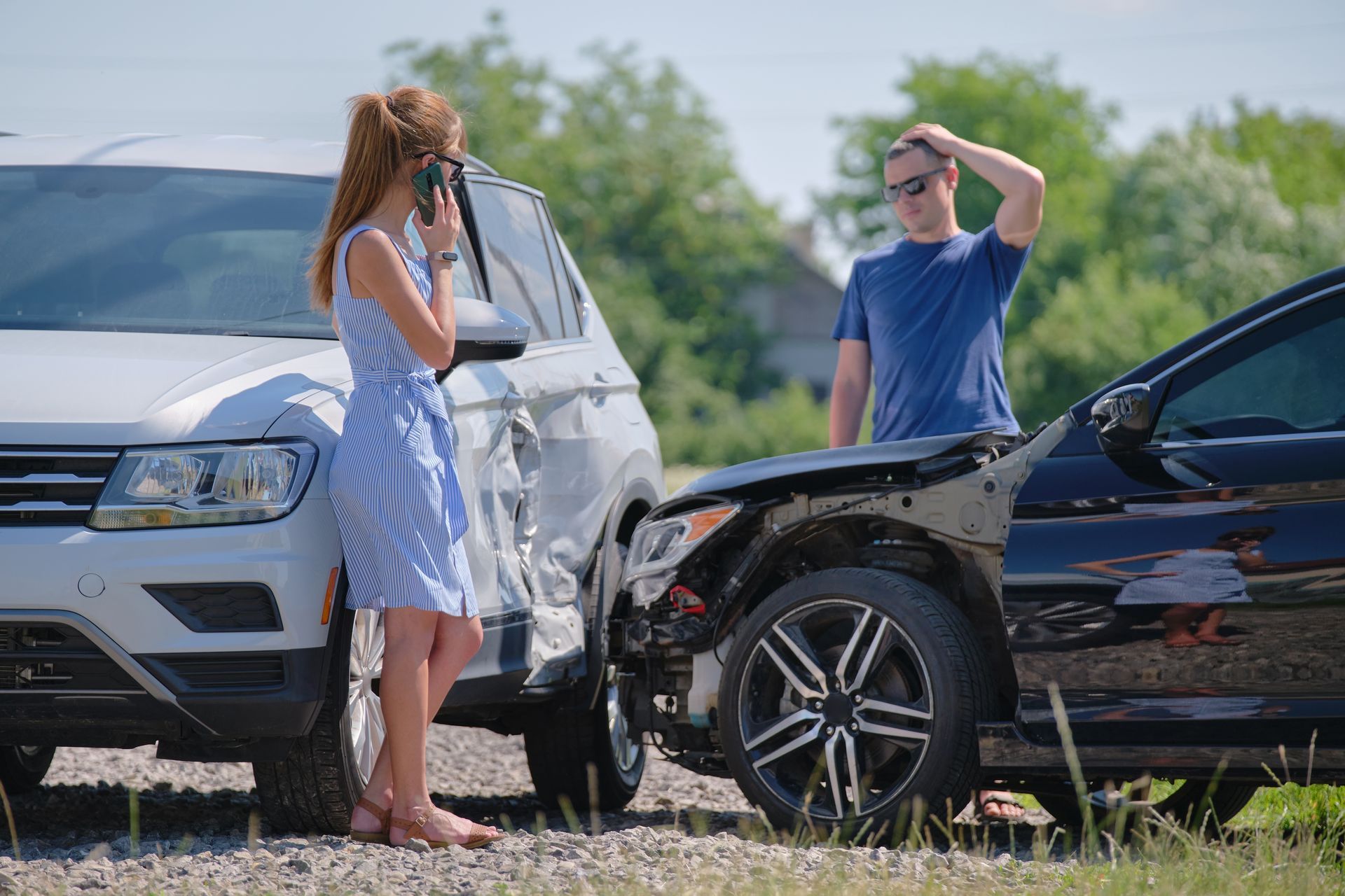 Two cars in a front-end collision; a woman and a man stand by the damaged vehicles on a roadside.
