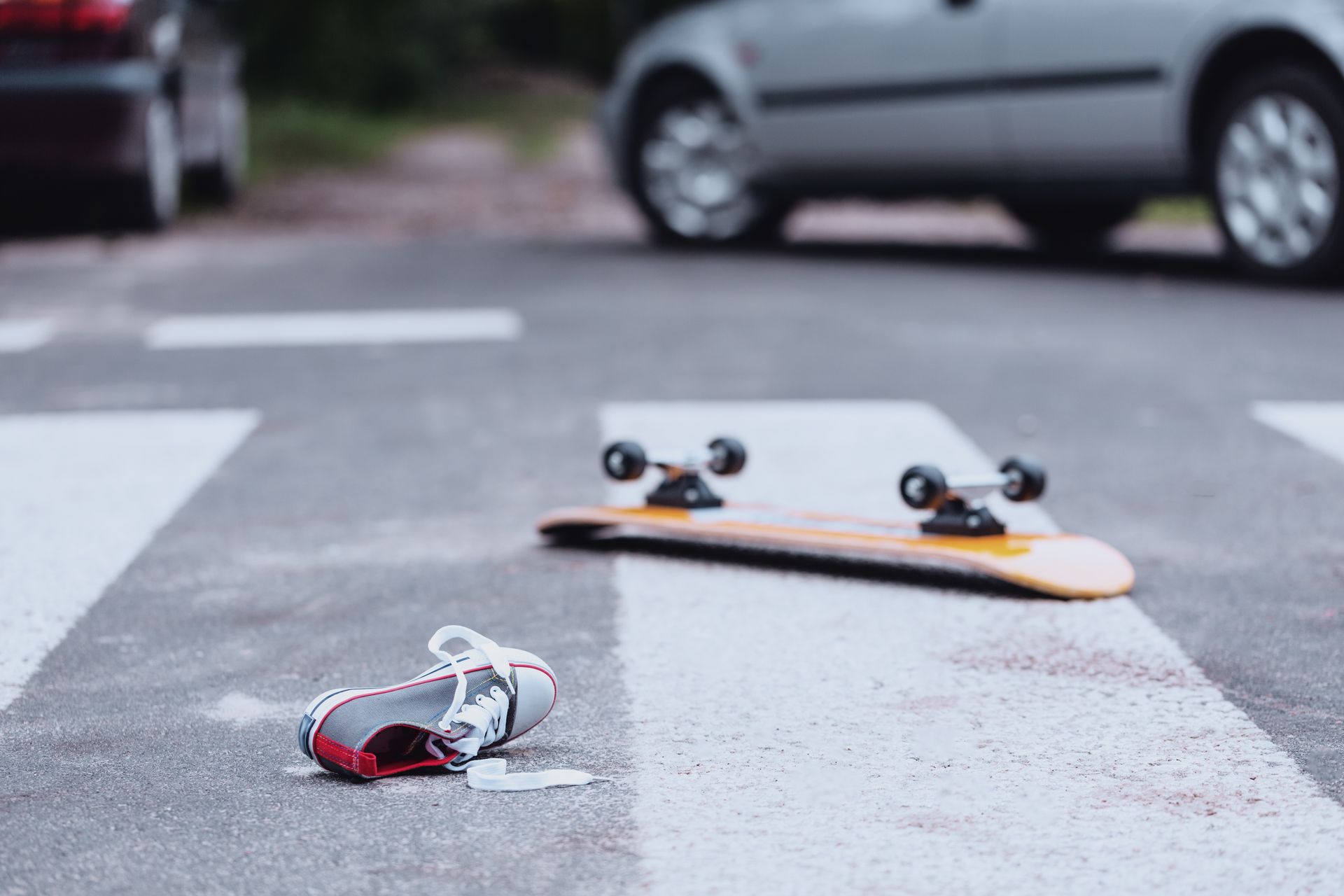 Skateboard and red earbuds lying on a crosswalk in front of a parked car.