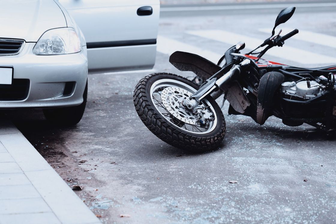Motorcycle on its side after crash beside a white car on wet pavement.